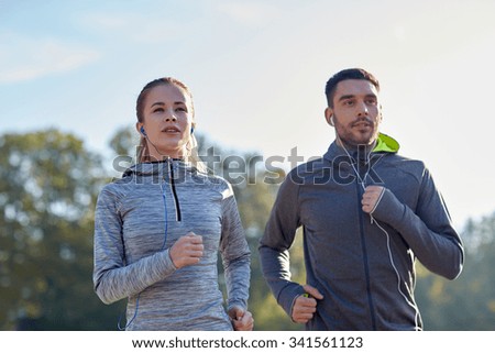 fitness, sport, people, technology and lifestyle concept - happy couple running and listening to music in earphones outdoors