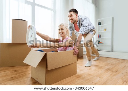 home, people, moving, time and real estate concept - happy couple having fun and riding in cardboard boxes with clock at new home