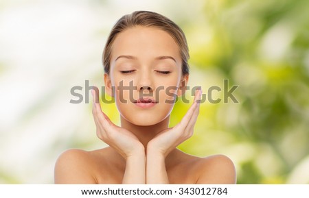 beauty, people, skincare and health concept - young woman face and hands over green natural background