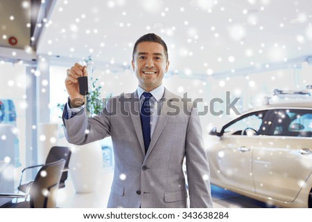 auto business, car sale, consumerism and people concept - happy man showing key at auto show or salon over snow effect