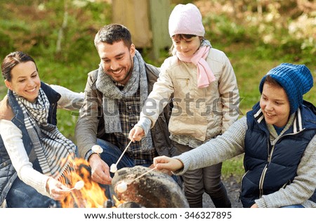 camping, travel, tourism, hike and people concept - happy family roasting marshmallow over campfire