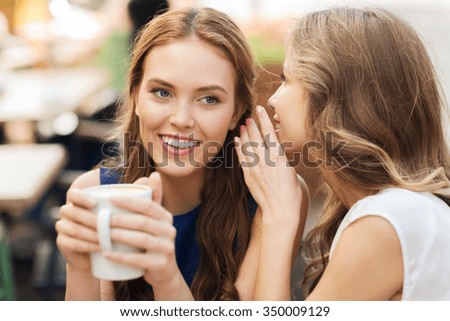 people communication and friendship concept - smiling young women drinking coffee or tea and gossiping at outdoor cafe