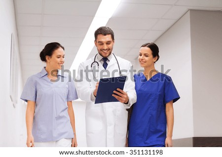 clinic, profession, people, health care and medicine concept - group of smiling medics or doctors with clipboard walking along hospital corridor