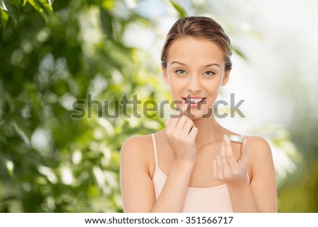 beauty, people and lip care concept - smiling young woman applying lip balm to her lips over green natural background