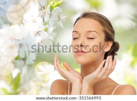 beauty, people, skincare, summer and health concept - young woman face and hands over green natural background with cherry blossom