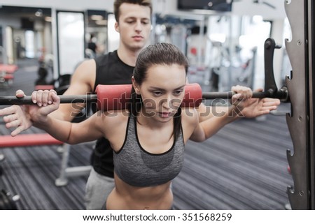 sport, fitness, teamwork, weightlifting and people concept - young woman and personal trainer with barbell flexing muscles in gym