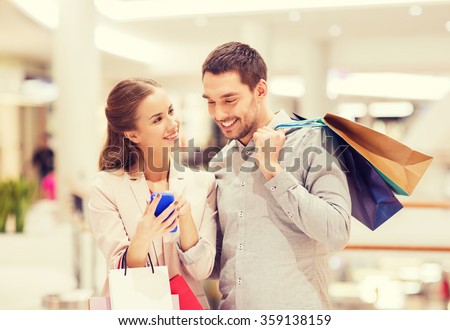 couple with smartphone and shopping bags in mall