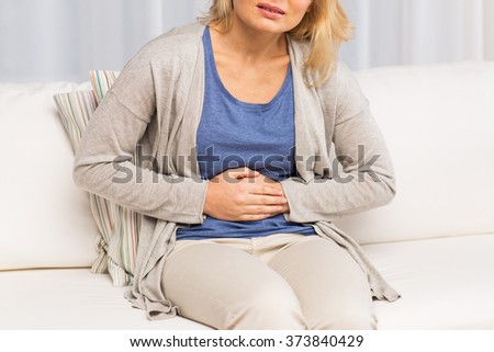 people, healthcare and problem concept - close up of unhappy woman suffering from stomach ache at home