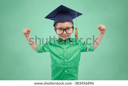 childhood, school, education, knowledge and people concept - happy boy in bachelor hat or mortarboard and eyeglasses showing strong hands over green school chalk board background