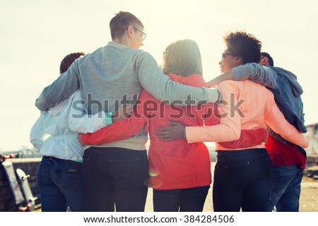 tourism, travel, people, leisure and teenage concept - group of happy friends hugging and talking on city street from back
