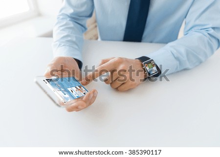 business, technology, mass media and people concept - close up of male hand holding and showing transparent smart phone and watch at office with news web page on screen