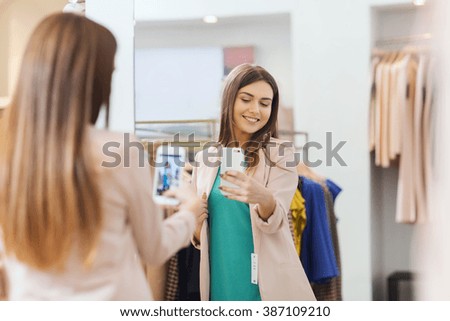 shopping, fashion, style, technology and people concept - happy woman with smartphone taking mirror selfie at clothing store
