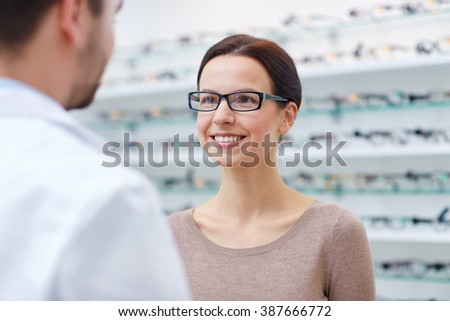 health care, people, eyesight and vision concept - happy woman in glasses looking and talking to optician at optics store