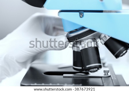 science, chemistry, biology, medicine and people concept - close up of scientist hand in glove setting microscope and making research in clinical laboratory
