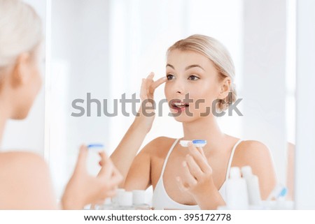 beauty, vision, eyesight, ophthalmology and people concept - young woman putting on contact lenses at mirror in home bathroom