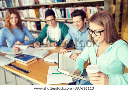 people, knowledge, education and school concept - group of happy students reading books, drinking coffee and preparing to exam in library
