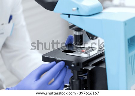 science, chemistry, biology, medicine and people concept - close up of scientist hands with microscope and blood test sample making research in clinical laboratory