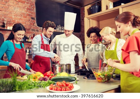 cooking class, culinary, food and people concept - happy group of friends and male chef cook cooking in kitchen