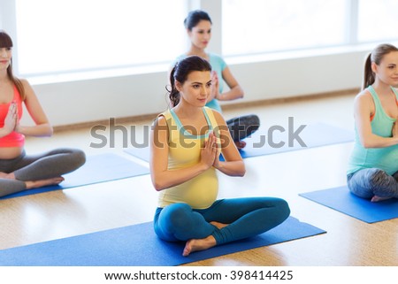 pregnancy, sport, fitness, people and healthy lifestyle concept - group of happy pregnant women exercising yoga in lotus pose in gym