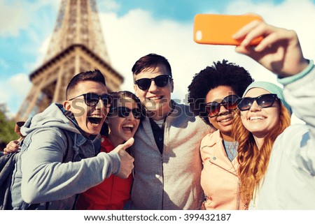 people, travel, tourism, friendship and technology concept - group of happy teenage friends taking selfie with smartphone and showing thumbs up over paris eiffel tower background
