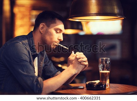 people, smoking and bad habits concept - man drinking beer and lighting cigarette at bar or pub
