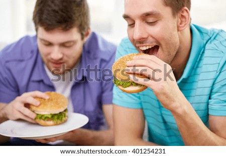 fast food, unhealthy eating, people and junk-food - close up of happy friends eating hamburgers at home