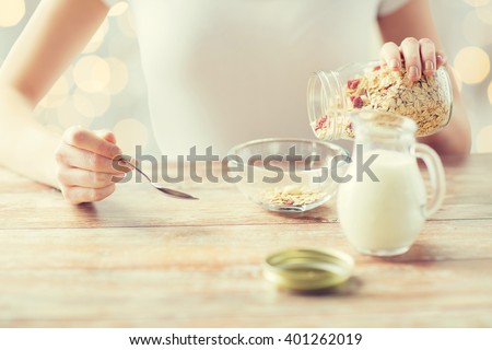 food, healthy eating, people and diet concept - close up of woman eating muesli with milk for breakfast over holidays lights background