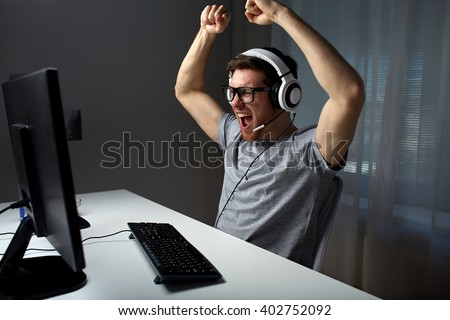 technology, gaming, entertainment, let\'s play and people concept - happy young man in eyeglasses with headset playing and winning computer game at home and streaming playthrough or walkthrough video