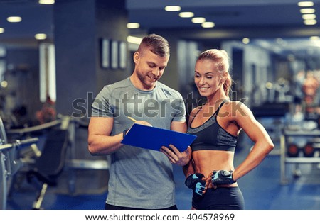 fitness, sport, exercising and diet concept - smiling young woman and personal trainer with clipboard writing exercise plan in gym