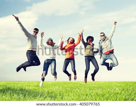 people, freedom, happiness and teenage concept - group of happy friends in sunglasses jumping high over blue sky and grass background