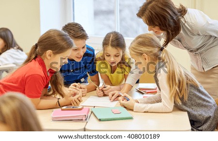 education, elementary school, learning and people concept - teacher helping school kids writing test in classroom