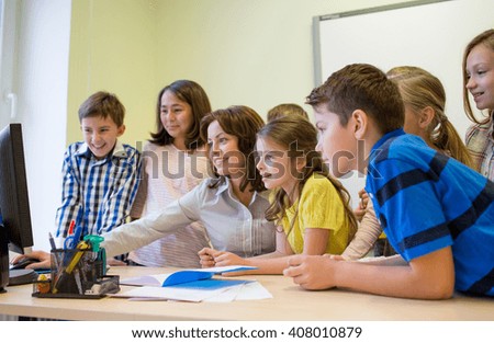 education, elementary school, learning, technology and people concept - group of school kids with teacher looking to computer monitor in classroom