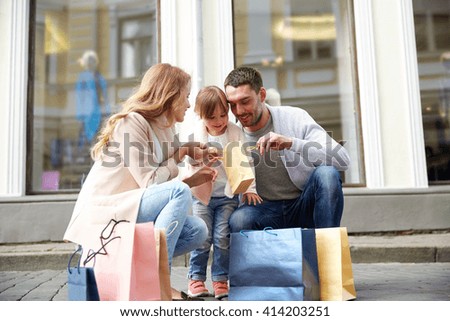 family, sale, consumerism and people concept - happy mother , father and little child with shopping bags reviewing purchases on city street