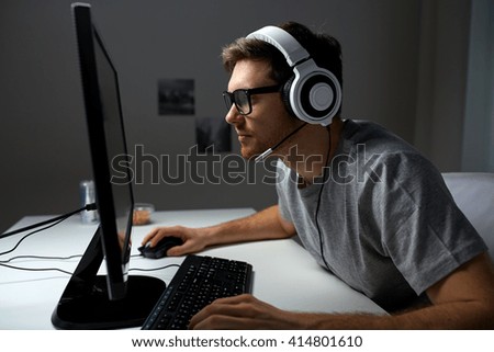 technology, gaming, entertainment, let\'s play and people concept - young man in headset and glasses with pc computer playing game at home and streaming playthrough or walkthrough video