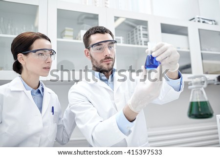 science, chemistry, technology, biology and people concept - young scientists with glass flask or test tube making research in clinical laboratory