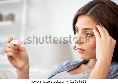 pregnancy, fertility, maternity and people concept - sad unhappy woman looking at pregnancy test at home