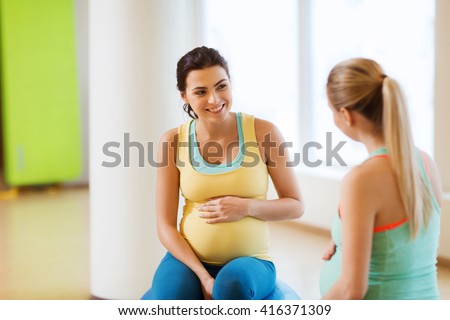 pregnancy, sport, fitness, people and healthy lifestyle concept - two happy pregnant women sitting and talking on balls in gym
