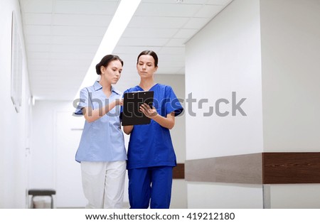 clinic, profession, people, health care and medicine concept - two medics or nurses with clipboard walking along hospital corridor