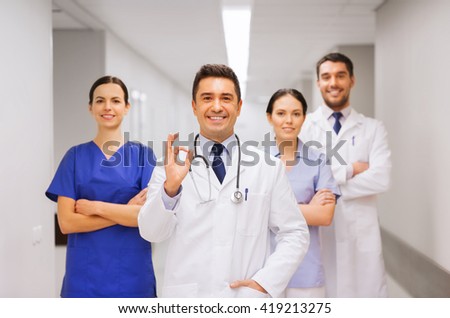 clinic, profession, people, health care and medicine concept - group of happy medics or doctors at hospital corridor showing ok hand sign