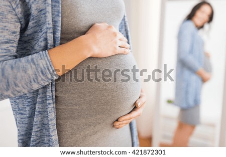 pregnancy, motherhood, people and expectation concept - close up of happy pregnant woman with big belly looking to mirror at home