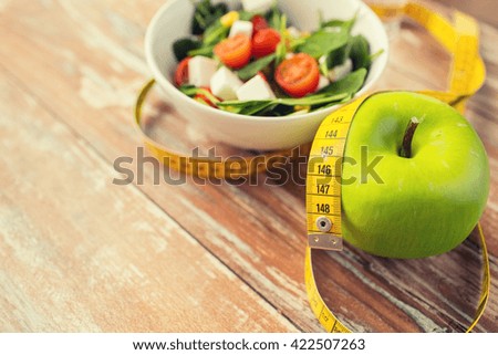 healthy eating, dieting, slimming and weigh loss concept - close up of green apple, measuring tape and salad