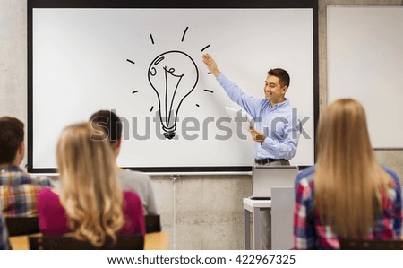 education, high school, teaching, idea and people concept - group of students and happy teacher with notepad showing light bulb drawing on white board in classroom