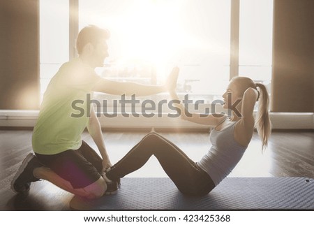 fitness, sport, training, teamwork and people concept - happy woman with personal trainer doing sit ups and high five gesture in gym