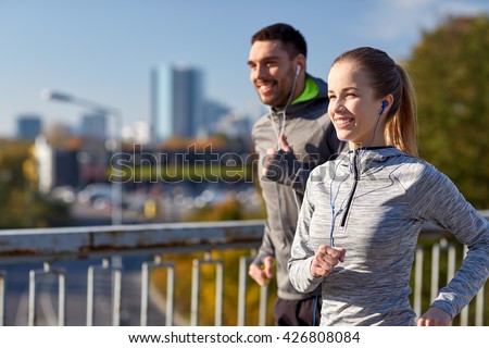 fitness, sport, people, technology and lifestyle concept - happy couple running and listening to music in earphones at city