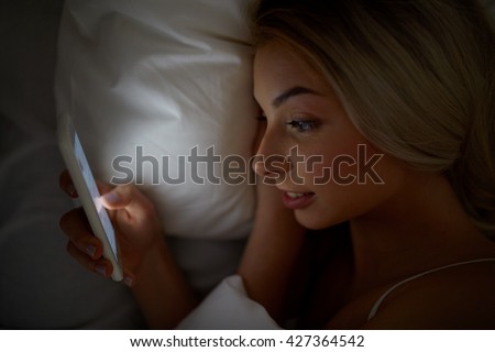 technology, internet, communication and people concept - happy smiling young woman texting on smartphone in bed at home bedroom at night