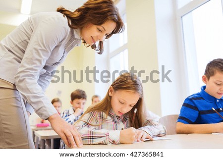 education, elementary school, learning and people concept - teacher helping school kids in classroom
