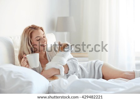 pets, morning, comfort, rest and people concept - happy young woman with coffee cup and cat in bed at home