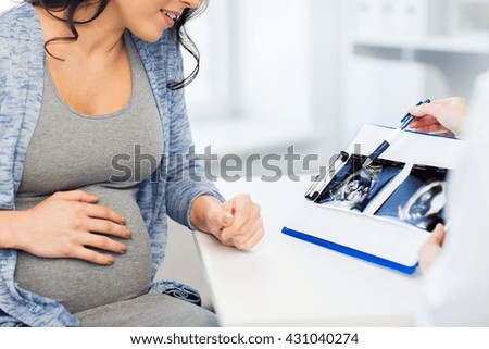 pregnancy, gynecology, medicine, health care and people concept - close up of gynecologist doctor showing ultrasound image on clipboard to pregnant woman at hospital