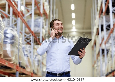 wholesale, logistic, business, export and people concept - smiling businessman with clipboard calling on smartphone at warehouse