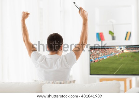 leisure, technology, mass media and people concept - happy man watching football or soccer game on tv and supporting team at home from back